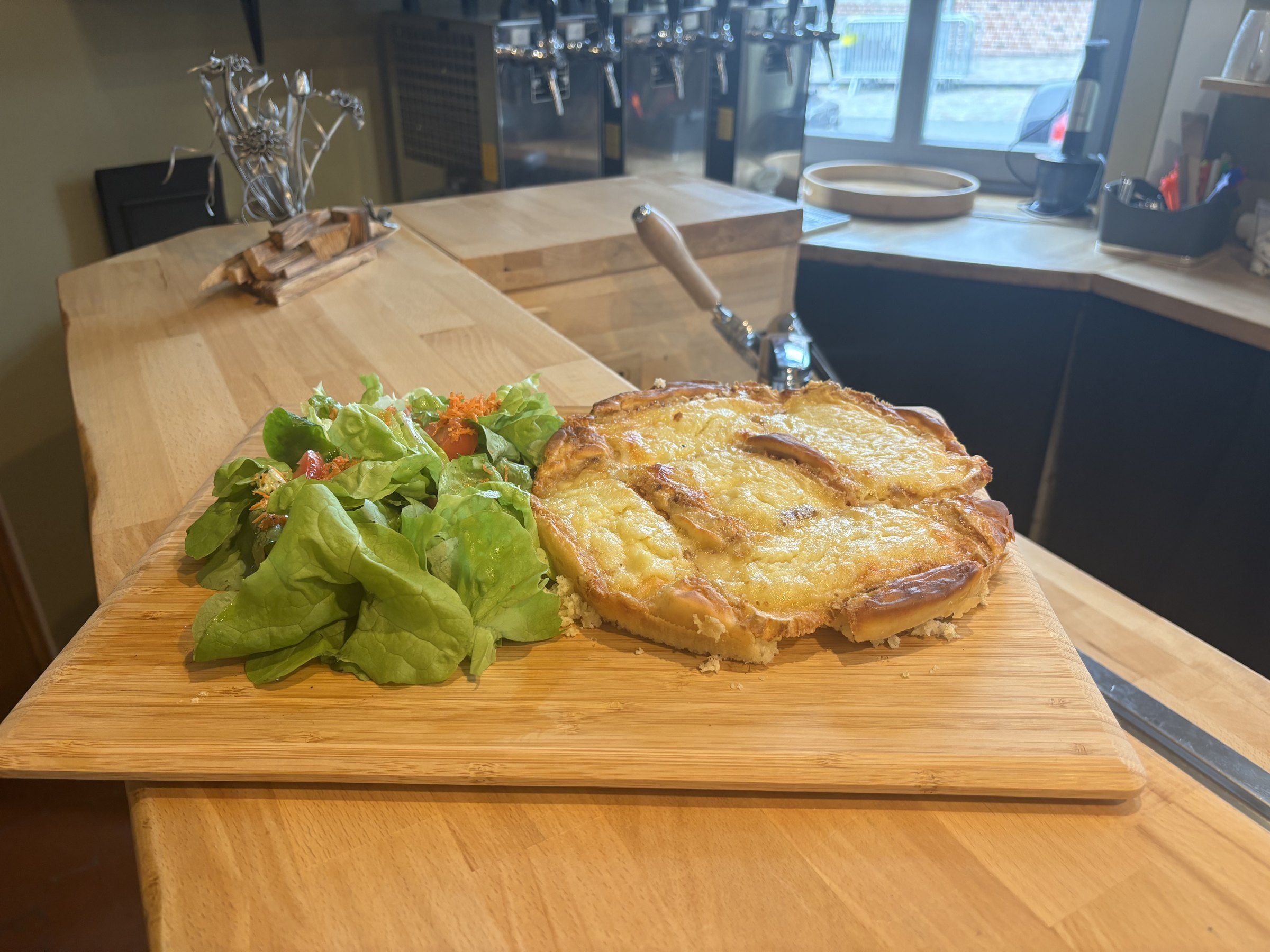 Planche flamiche au Maroilles servie avec une salade, sur le comptoir en bois de la brasserie